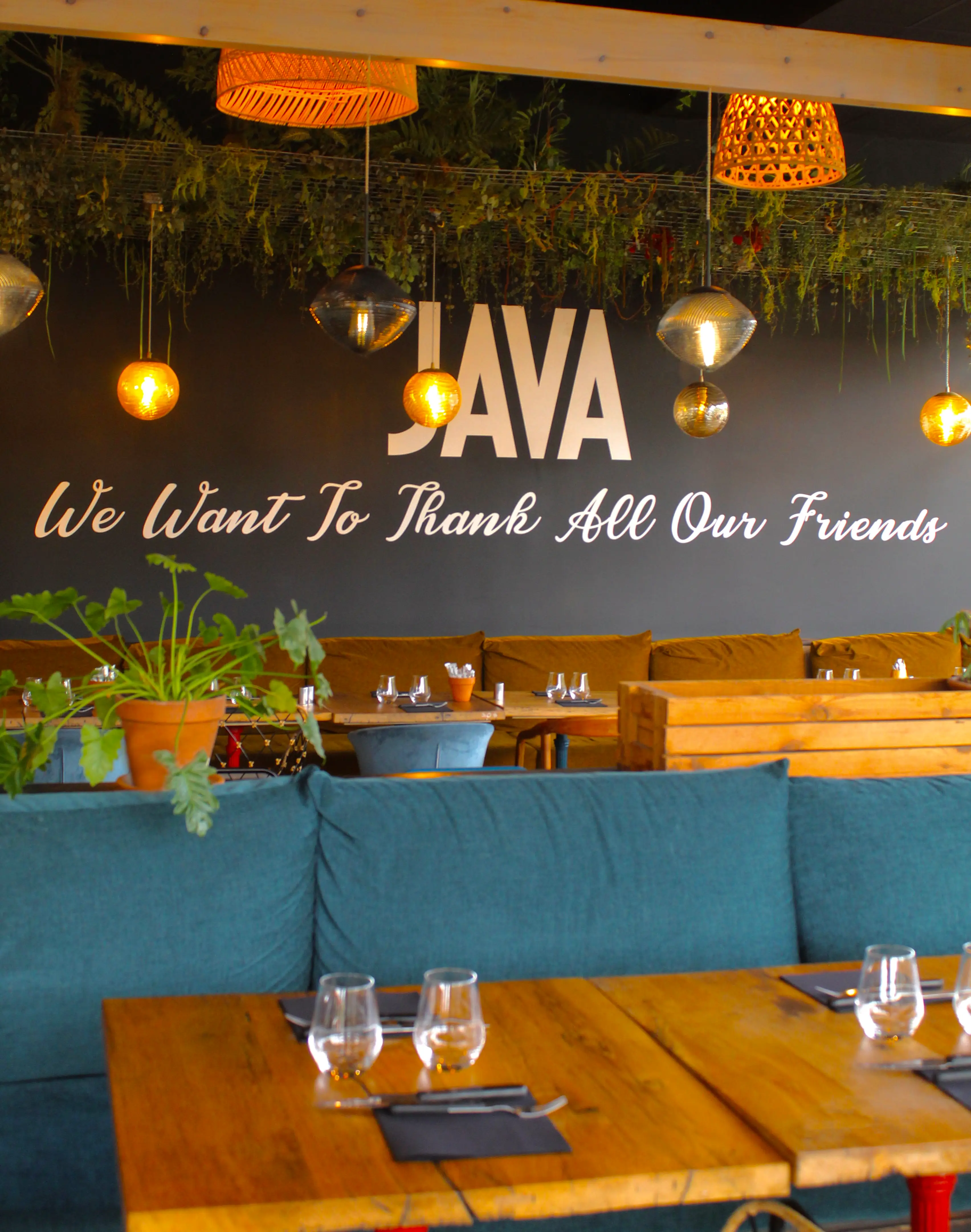 Mur signature du restaurant JAVA : « We want to thank all our friends », plantes suspendues et banquettes moutarde